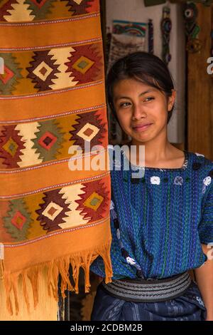 Eine attraktive junge Frau Maya tragen typische Kleid sieht vor die Tür einer Familie Weberei in San Antonio Palopó, Guatemala. Stockfoto