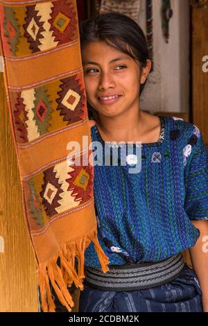 Eine attraktive junge Frau Maya tragen typische Kleid sieht vor die Tür einer Familie Weberei in San Antonio Palopó, Guatemala. Stockfoto