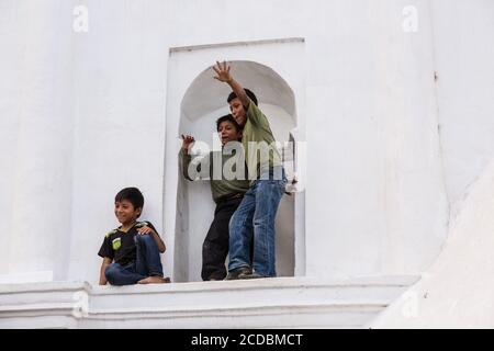 Drei Jungs Clown herum, während ein Programm vor der Kirche in San Antonio Palopo, Guatemala. Sie sind auf einer Kante auf dem chur aufgestiegen Stockfoto