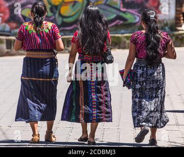 Drei junge Tzutujil Maya-Frau in traditioneller Kleidung spazieren entlang einer Straße in San Juan la Laguna, Guatemala. Stockfoto