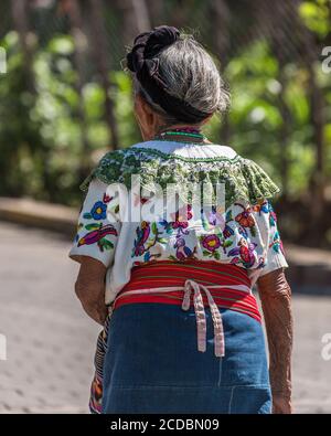 Eine elderlyTzutujil Maya Frau in traditioneller Kleidung geht die Straße hinunter in San Pablo la Laguna, Guatemala. Stockfoto