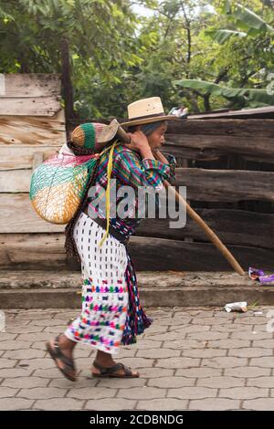 Ein älterer Maya-Bauer in traditioneller Kleidung aus San Pedro la Laguna, Guatemala, kehrt von der Arbeit auf den Feldern nach Hause zurück, mit seiner Hacke und einer Last auf seiner Stockfoto