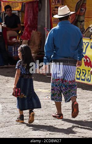 Ein Tzutujil Vater und Tochter in traditionellen Kleidern Spaziergang auf dem wöchentlichen offenen Markt in Santiago Atitlan, Guatemala. Stockfoto