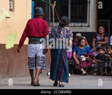 Ein älteres Tzutujil Maya-Paar in traditioneller Kleidung hält die Hände, während sie auf dem wöchentlichen offenen Markt in Santiago Atitlan, Guatemala, spazieren gehen. Stockfoto