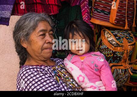 Eine ältere Tzutujil Maya-Frau in traditioneller Kleidung hält ihre kleine Enkelin in einem Geschäft in Santiago Atitlan, Guatemala. Stockfoto