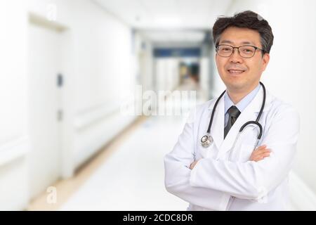 Ein asiatischer Arzt mittleren Alters lächelt im Krankenhausflur. Stockfoto