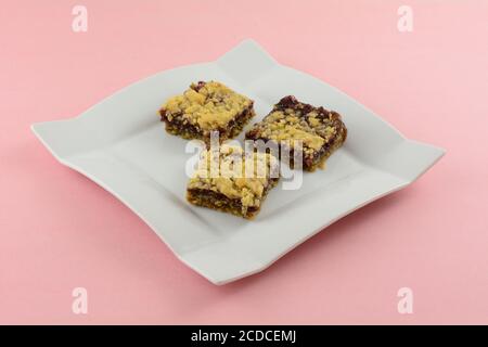 Drei gebackene Himbeer-Hafer-Krümel-Quadrate auf weißem Dessertteller Auf rosa Hintergrund Stockfoto