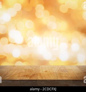 Leerer Holztisch und verschwommener heller goldener Hintergrund mit Lichtern und Bokeh, Fokus auf die Tischplatte Stockfoto