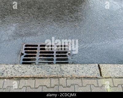 Metall-Sturmabfluss auf der Straße. Regenwasser aus heftigem Regen fließt in einen Sturmabfluss Stockfoto