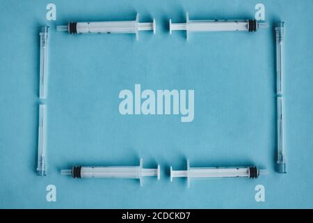 Ein Rahmen von Spritzen und Nadeln isoliert auf einem blauen Hintergrund. Coronavirus-Impfstoff. Pandemie- und Behandlungskonzept. Bluttest. Modell, Platz für Text Stockfoto