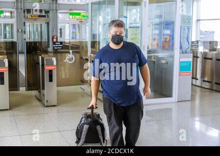 Mann Reisende mit Koffer auf Rädern trägt Schutzmaske während Pandemieausbruch afraids des gefährlichen Influenza-Coronavirus COVID-19 stellt bei Plattform Stockfoto