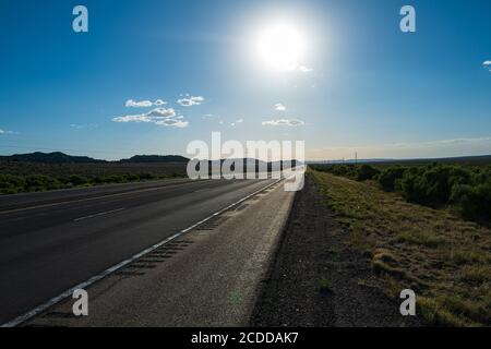 Klassischer Panoramablick auf eine endlose gerade Straße, die durch die karge Landschaft des amerikanischen Südwestens führt. Stockfoto