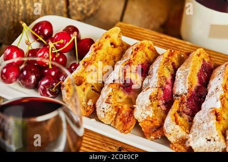 Kirschkuchen in Scheiben geschnitten auf einem weißen Teller mit Kirschen und einem Glas Rotwein. Stockfoto