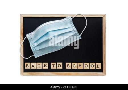 Zurück zur Schule Wörter Schriftzug auf der Schule schwarze Kreidetafel. Medizinische Maske auf dem Hintergrund der Tafel. Das Konzept der sozialen Distanz. Flach Stockfoto