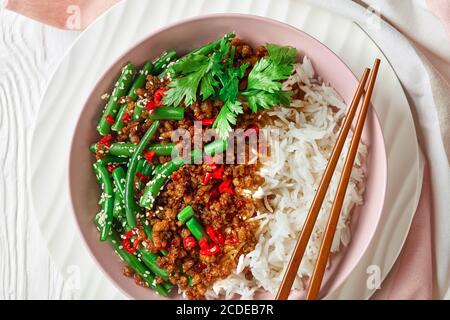 Vietnamesischer Stil gehacktes Schweinefleisch mit Reis und grünen Bohnen rühren braten bestreut mit Sesam, Chili-Pfeffer auf der Oberseite, serviert auf einer rosa Schüssel mit Essstäbchen Stockfoto