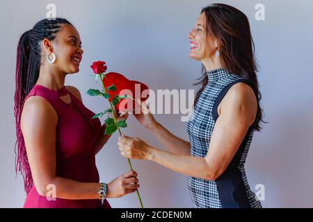 Schöne Mutter Geschenk rote Rose und rotes Herz zu ihrer Tochter im Haus. Liebe Feier. Stockfoto