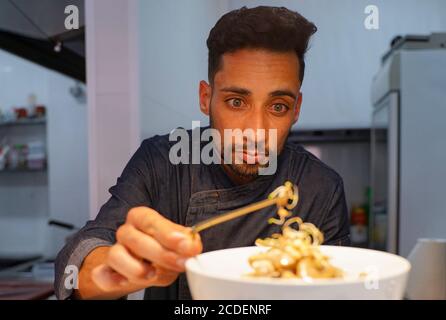 Nahaufnahme eines konzentrierten männlichen Küchenchefs, der Essen in der Küche garniert. Kaukasischer Chefkoch garniert köstliche Desserts auf einem Teller im Hotel. Gesicht fokussieren Stockfoto