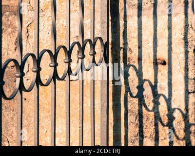 Detailansicht des dekorativen schmiedeeisernen Tores und des Schattens an der Wand. Stockfoto