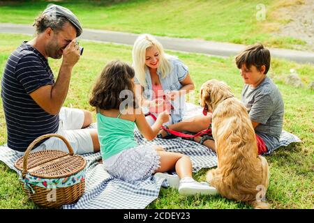 Familie im Park für ein Picknick im Sommerurlaub. Vater macht ein Foto mit seiner Vintage-Fotokamera. Konzentrieren Sie sich auf das Gesicht des Vaters. Reisen, Elternschaft Stockfoto