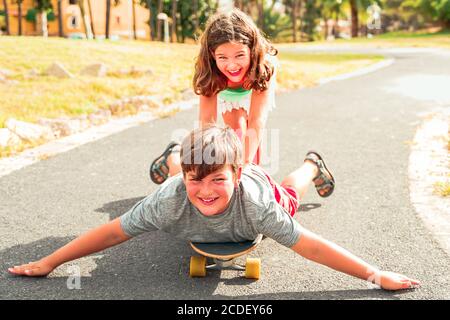 Schwester und Bruder spielen mit Longboard im Park. Junge Menschen glücklich in einem perfekten Sommer. Urlaub, Sport und jüngere Konzept. Konzentriere dich auf den Jungen Stockfoto