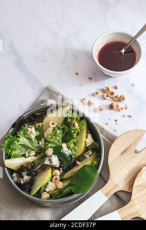 Salatschüssel mit gemischten Salatblättern, Birnenscheiben, gerösteten Haselnüssen, krümeligen Blauschimmelkäse und Brombeer-Dressing. Stockfoto