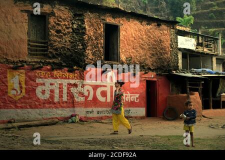 Ein Kind, das am Straßenrand steht und einen Wasserkrug trägt, während es auf ein Fahrzeug in der ländlichen Gegend von Gandaki Pradesh in Nepal achtet. Stockfoto