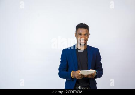 Junger gutaussehender afrikanischer Geschäftsmann hält eine Tablette und lächelt Stockfoto