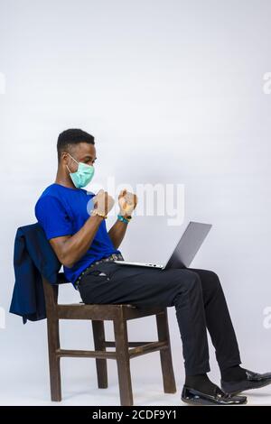 Junger schöner afrikanischer Geschäftsmann trägt eine Maske aufgeregt über was Er sah auf seinem Tablet Stockfoto