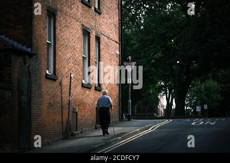 Älterer Mann, der mit Stock in Preston, Lancashire, Großbritannien, läuft. Stockfoto