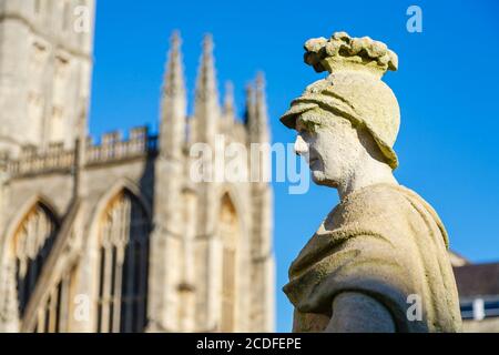 Verwitterte Kalksteinstatue auf der Terrasse der berühmten römischen Bäder in Bath, Somerset, Südwestengland mit Bath Abbey dahinter Stockfoto