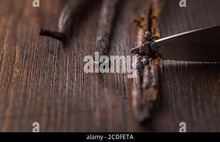 Vanilleschoten und Samenschoten mit Messer auf Holzhintergrund. Zubereitung von Vanille als Backzutat. Stockfoto