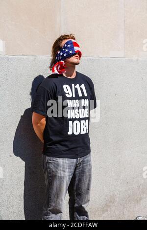 Ein junger amerikanischer Mann steht mit verbundenen Augen am World Trade Center in New York und trägt ein schwarzes T-Shirt mit der Aufschrift: "9/11 war ein Innenjob!" Stockfoto