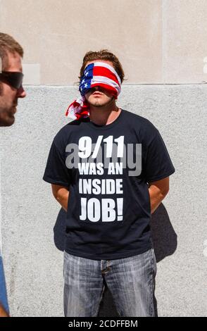 Ein junger amerikanischer Mann steht mit verbundenen Augen am World Trade Center in New York und trägt ein schwarzes T-Shirt mit der Aufschrift: "9/11 war ein Innenjob!" Stockfoto