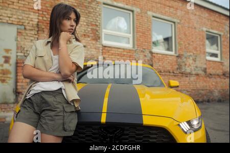 Mädchen steht in der Nähe von gelben Auto mit dem Autobot-Logo oder Roboter Transformator. Stockfoto