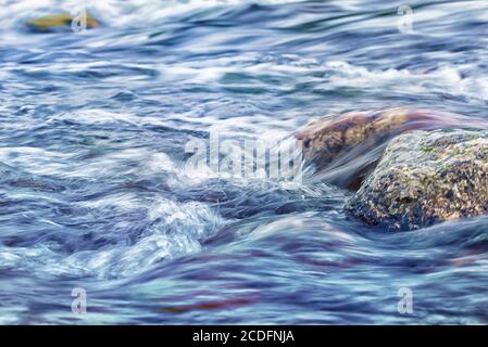 Steine in wild fließenden Fluss. Landschaftsfoto mit Langzeitbelichtung, die das Konzept des Flüssigkeitsflusses darstellt Stockfoto