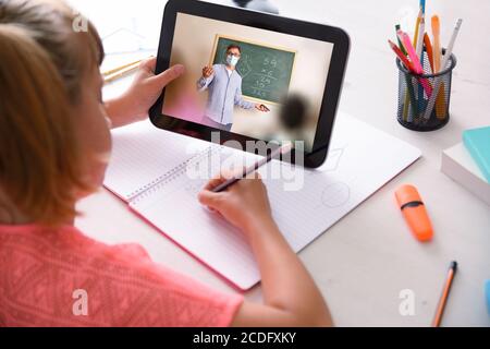 Schulmädchen im Anschluss an den Online-Schulkurs mit einem Tablet in Quarantäne im heimischen Lernraum. Erhöhte Rückansicht. Stockfoto