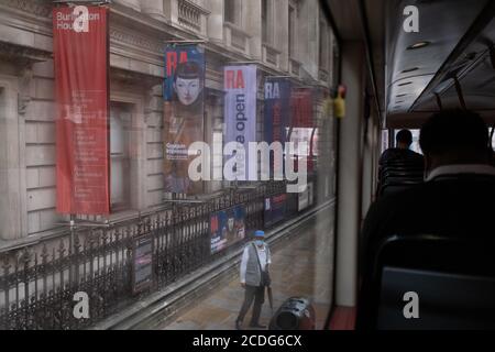 Busreisende sehen einen Mann mit Gesichtsbedeckung, der unter Spruchbändern für die Gauguin-Sommerausstellung der Royal Academy während der Coronavirus-Pandemie am 27. August 2020 in London, England, steht. Stockfoto