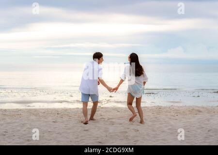 Asiatische Paar in der Liebe mit romantischen zarten Momente laufen und Hand halten am Strand zwischen Sonnenuntergang in Thailand. Stockfoto