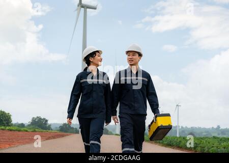 Asiatische Mann und Frau Inspektionsingenieure Vorbereitung und Fortschrittskontrolle mit digitalen Tablet einer Windkraftanlage mit Sicherheit in Windpark in Thailand. Stockfoto