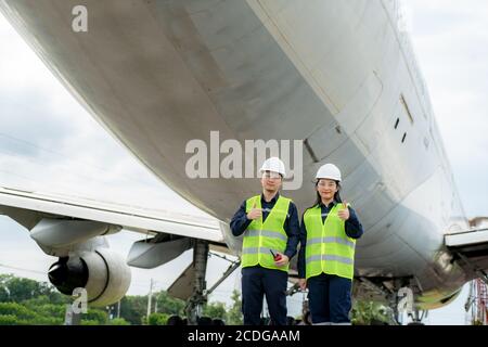 Asiatische Mann und Frau Ingenieur Wartung Flugzeug Daumen nach oben und halten Schlüssel vor Flugzeug von Reparaturen, Fixes, Modernisierung und Renovierung in einem Stockfoto