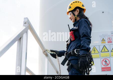 Asiatin Inspektionsingenieur mit Sicherheitsgurt und Sicherheitsleine Arbeitsvorbereitung und Fortschrittskontrolle einer Windenergieanlage mit Sicherheit im Windpark Stockfoto