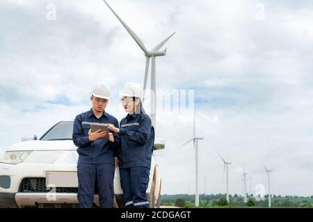 Asiatische Mann und Frau Inspektionsingenieure Vorbereitung und Fortschrittskontrolle mit digitalen Tablet einer Windkraftanlage mit Sicherheit in Windpark in Thailand. Stockfoto