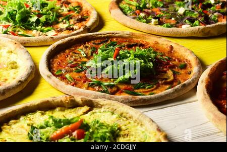 Pizzakreise mit Fleisch, grünen Zwiebeln, Tomaten und Salat auf Holzgrund. Fast-Food-Restaurant-Konzept. Nehmen Sie Lebensmittel mit verschiedenen Zutaten und knackigen Kanten. Verschiedene Pizzabücken für die Speisekarte Stockfoto
