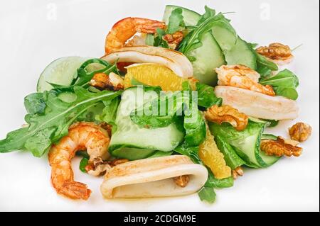 Vegetarischer roher Salat aus Meeresfrüchten mit Gurken und Orangenscheiben, Rucola, Garnelen, Tintenfischringen und Walnüssen auf Weiß isoliert Stockfoto