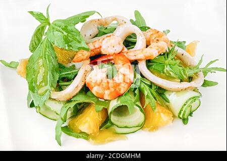 Grüner Salat aus Bio-Meeresfrüchten mit Garnelen, Tintenfischringen, Gurken und Rucola, verziert mit Basilikumblättern Stockfoto