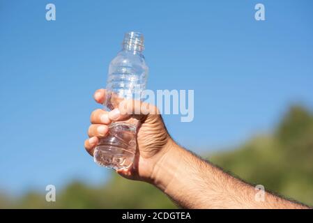 Hand des Mannes hält eine Flasche Wasser gegen den blauen Himmel Stockfoto