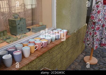 Bunte Tassen und Tassen zum Verkauf im Fensterbrett des kleinen Eck-Shops mit Antiquitäten in Freiburg im Breisgau in Deutschland ausgestellt. Stockfoto