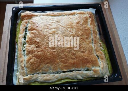 Blätterteig mit Spinat, Feta und Eiern gewürzt mit Oregano, Salz, schwarzem Pfeffer, Muskatnuss und fein gehackter Zwiebel auf rechteckigem Backblech gebacken. Stockfoto