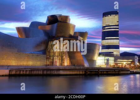 Bilbao, Spanien - 15. Dezember 2011: Das Guggenheim Museum Bilbao, Spanien unter einem dramatischen Sonnenuntergangshimmel. Im Hintergrund ist die neueste Ergänzung zu Bilbao Stockfoto