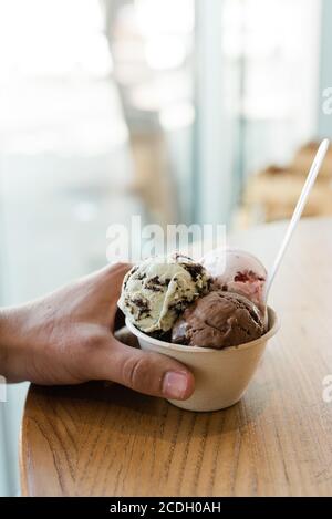 Mann hält eine Tasse Schokolade, Erdbeere und Minze Schokolade Chip Eis auf einem Holztisch Stockfoto